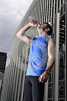 Young sport man drinking water bottle after running training session in business district