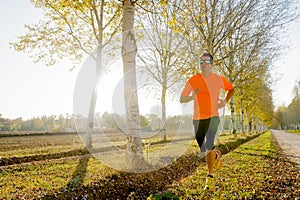 Young sport man running outdoors in off road trail ground with trees under beautiful Autumn sunlight