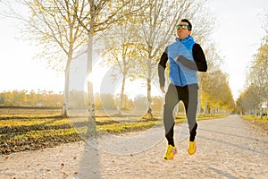 Young sport man running outdoors in off road trail ground with trees under beautiful Autumn sunlight