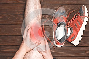 Young sport man with strong athletic legs holding knee with his hands in pain after suffering ligament injury during a running