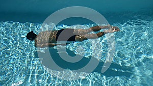 Young sport man with toned body swimming underwater in swimming pool with crystal clear water. summer season at tropical area