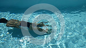 young sport man with toned body swimming underwater in swimming pool with crystal clear water. summer season at tropical area