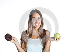 Young sport woman holding apple and chocolate donut in her hands in healthy fruit versus sweet junk food temptation