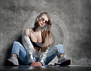 Young sport woman after workout exercise sitting under snow in silver thin down puffer jacket blue jeans