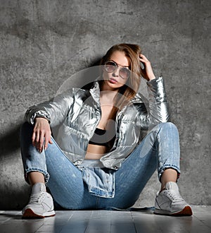 Young sport woman after workout exercise sitting under snow in silver thin down puffer jacket blue jeans