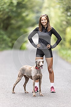 Young sporting woman and her Weimaraner dog stand together in the forest.