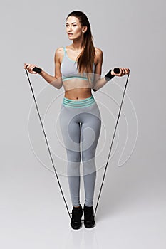 Young sportive beautiful girl doing exercises with jumping rope over white background.