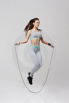 Young sportive beautiful girl doing exercises with jumping rope over white background.