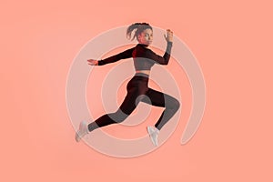 Young sportive black woman training on red neon studio background, running and looking at camera, full length