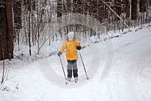 Young sportive girl running on skies in winter road in forest, full-length, copys pace