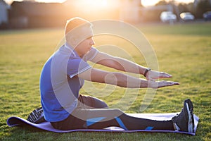 Young sportive man doing stretching exercises before running in morning field outdoors