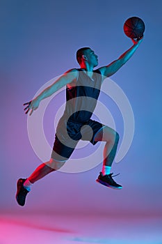 Young sportive man playing basketball isolated on blue studio background in neon light. Youth, hobby, motion, activity