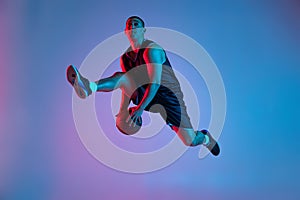 Young sportive man playing basketball isolated on blue studio background in neon light. Youth, hobby, motion, activity