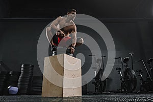 Young sportive man resting after box jump exercise at the gym