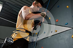 Young sportive man, rock climber holding rope, ready for training on the artificial climbing wall. Concept of sport life