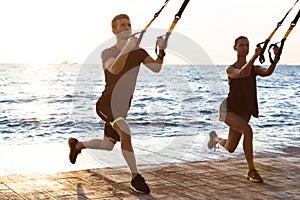 Young sportive people training with trx near sea in the morning.