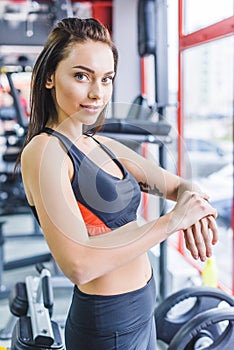young sportive woman checking fitness tracker at gym and looking