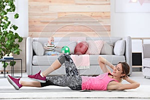 Young sportive woman doing exercise while her son sitting on sofa at home