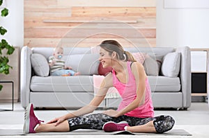 Young sportive woman doing exercise while her son sitting on sofa at home