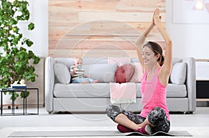 Young sportive woman doing exercise while her son sitting on sofa at home, space for text.