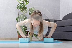 Young sportive woman doing exercise at home using yoga blocks. Girl does yoga with bricks