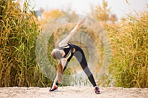 Young sportive woman doing exercises in autumn. Sportswoman stretching her body.