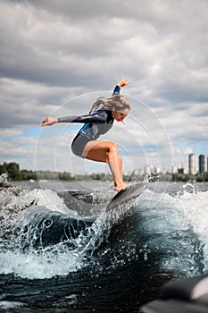 Young sportive woman effectively jumps on the wave on surfboard