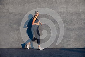 Young sportive woman jumping and running on gray background, female model in sportswear exercising outdoors