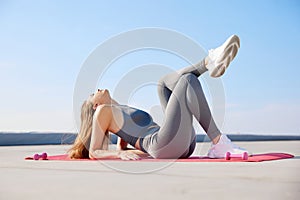 Young sportive woman, keeping body in tune, doing stretching exercises on warm sunny day outdoors. Resting