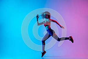 Young sportive woman running isolated on gradient pink-blue studio background in neon light.