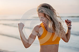 Young sportive woman showing her muscles at beach.