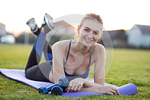 Young sportive woman in sports clothes laying on training mat before doing exercises in field at sunrise