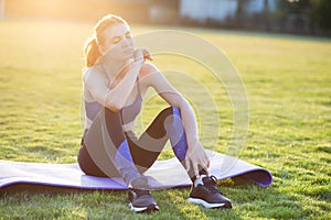 Young sportive woman in sports clothes sitting on training mat before doing exercises in field at sunrise