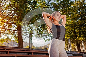 Young sportive woman tying her hair into pony tail on sportsground in summer. Preparation for workout