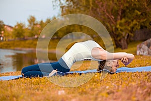 A young sports girl practices yoga on a fall yellow lawn by the river, use yoga asana posture. Meditation and unity with nature