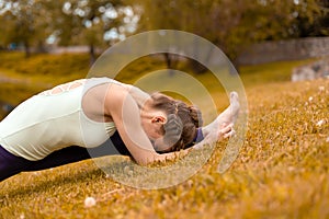 A young sports girl practices yoga on a fall yellow lawn by the river, use yoga assans posture. Meditation and unity with nature