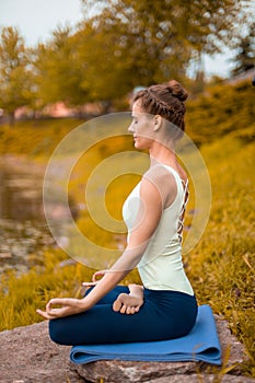 A young sports girl practices yoga on a fall yellow lawn by the river, use yoga assans posture. Meditation and unity with nature