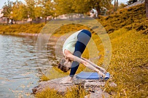 A young sports girl practices yoga on a fall yellow lawn by the river, use yoga assans posture. Meditation and unity with nature