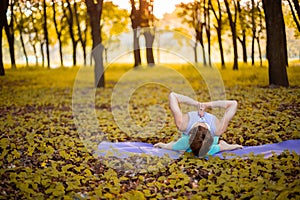 A young sports girl practices yoga in a quiet green forest in autumn at sunset, in a yoga asana pose. Meditation and oneness with photo