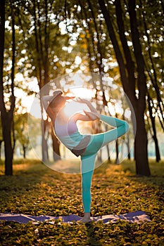 A young sports girl practices yoga in a quiet green forest in autumn at sunset, in a yoga asana pose. Meditation and oneness with