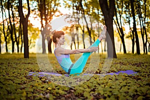 A young sports girl practices yoga in a quiet green forest in autumn at sunset, in a yoga asana pose. Meditation and oneness with