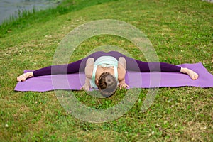 A young sports girl practices yoga in a quiet location on the river bank in summer, in a yoga asana pose. Meditation and oneness