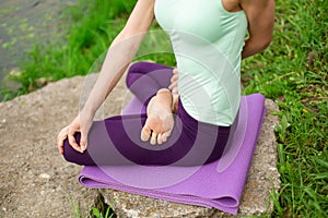 A young sports girl practices yoga in a quiet location on the river bank in summer, in a yoga asana pose. Meditation and oneness