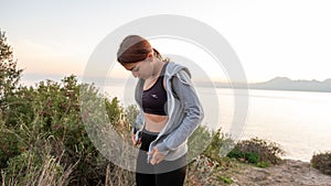 Young sports girl putting on after exercise by the sea over huge cliffs at sunset. She wears tights and sports bra