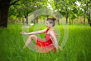 Young sports girl in a red dress practices yoga in a quiet green forest. Meditation and oneness with nature