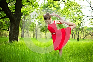 Young sports girl in a red dress practices yoga in a quiet green forest. Meditation and oneness with nature