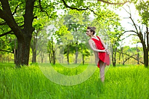 Young sports girl in a red dress practices yoga in a quiet green forest. Meditation and oneness with nature