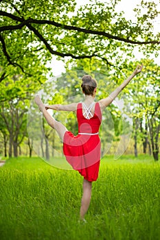 Young sports girl in a red dress practices yoga in a quiet green forest. Meditation and oneness with nature