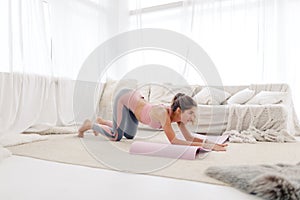 Young sports girl in sportswear is doing yoga and stretching at home in a bright room.