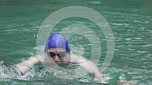 The young sports man floats in the pool a breast stroke on the camera,.slow motion